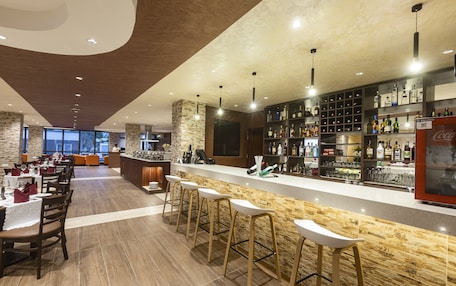 A modern bar area with a long counter, multiple stools, and a variety of bottles.