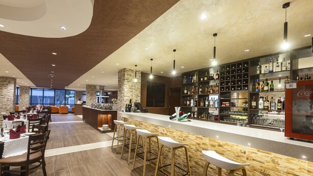A modern bar area with a long counter, multiple stools, and a variety of bottles.