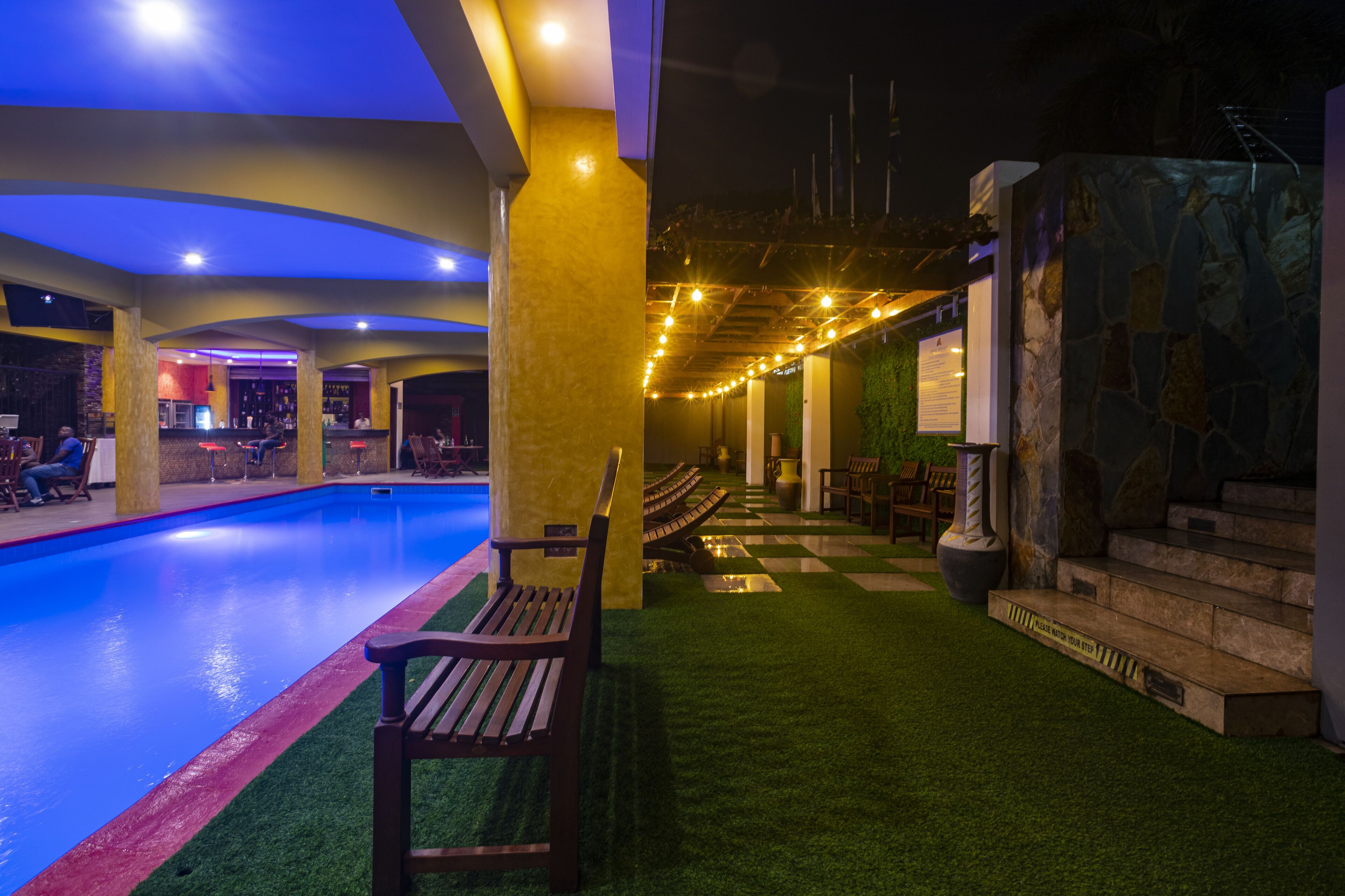A pool area with artificial grass, a wooden bench, and a stone wall with steps.