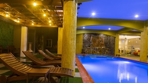 A pool area with lounge chairs, a stone wall, and a ceiling with exposed beams and lights.