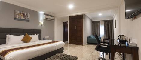 A hotel room with a large bed, a desk, a chair, and a TV.