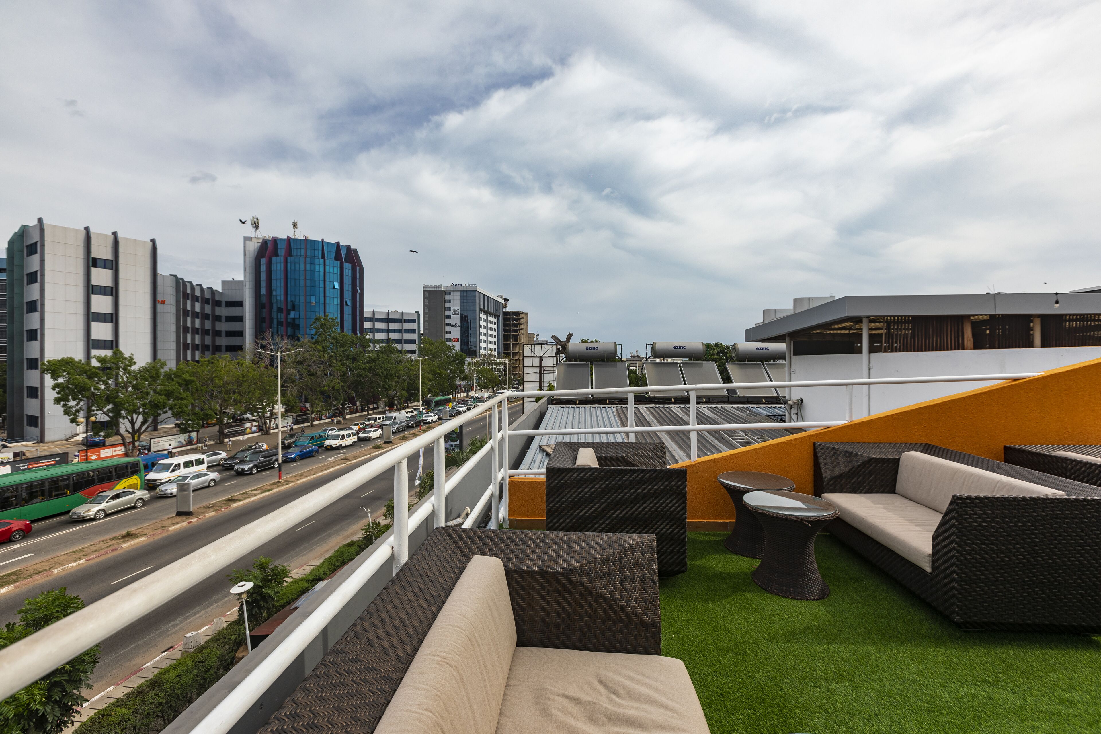 A rooftop lounge with outdoor seating, a view of a cityscape, and a road with vehicles.