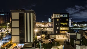 A multi-story hotel with a modern design, featuring a rooftop terrace and a parking area.