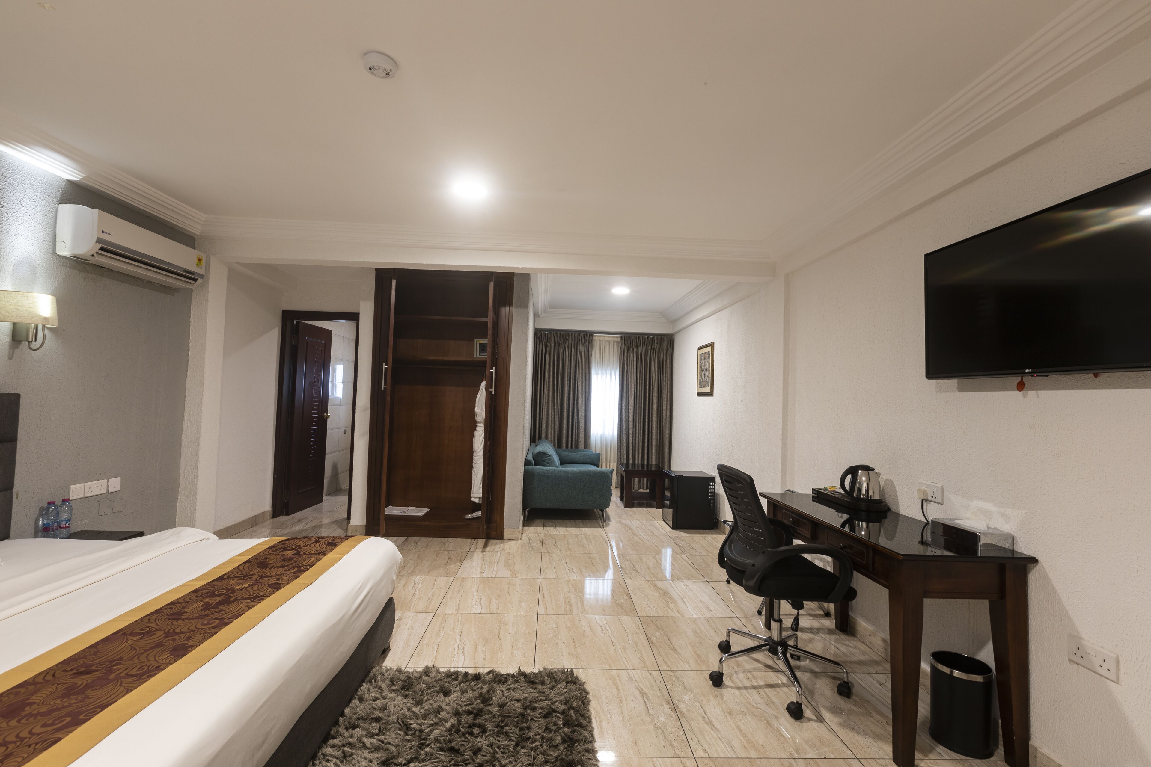 Habitación de hotel con cama, escritorio, silla, televisión y baño visible a través de una puerta abierta.