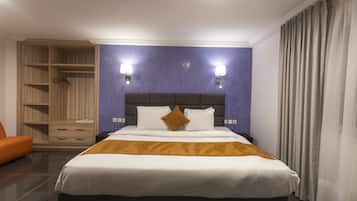 Une chambre d’hôtel comprenant un lit, une armoire, un coin salon et deux lampes fixées au mur.