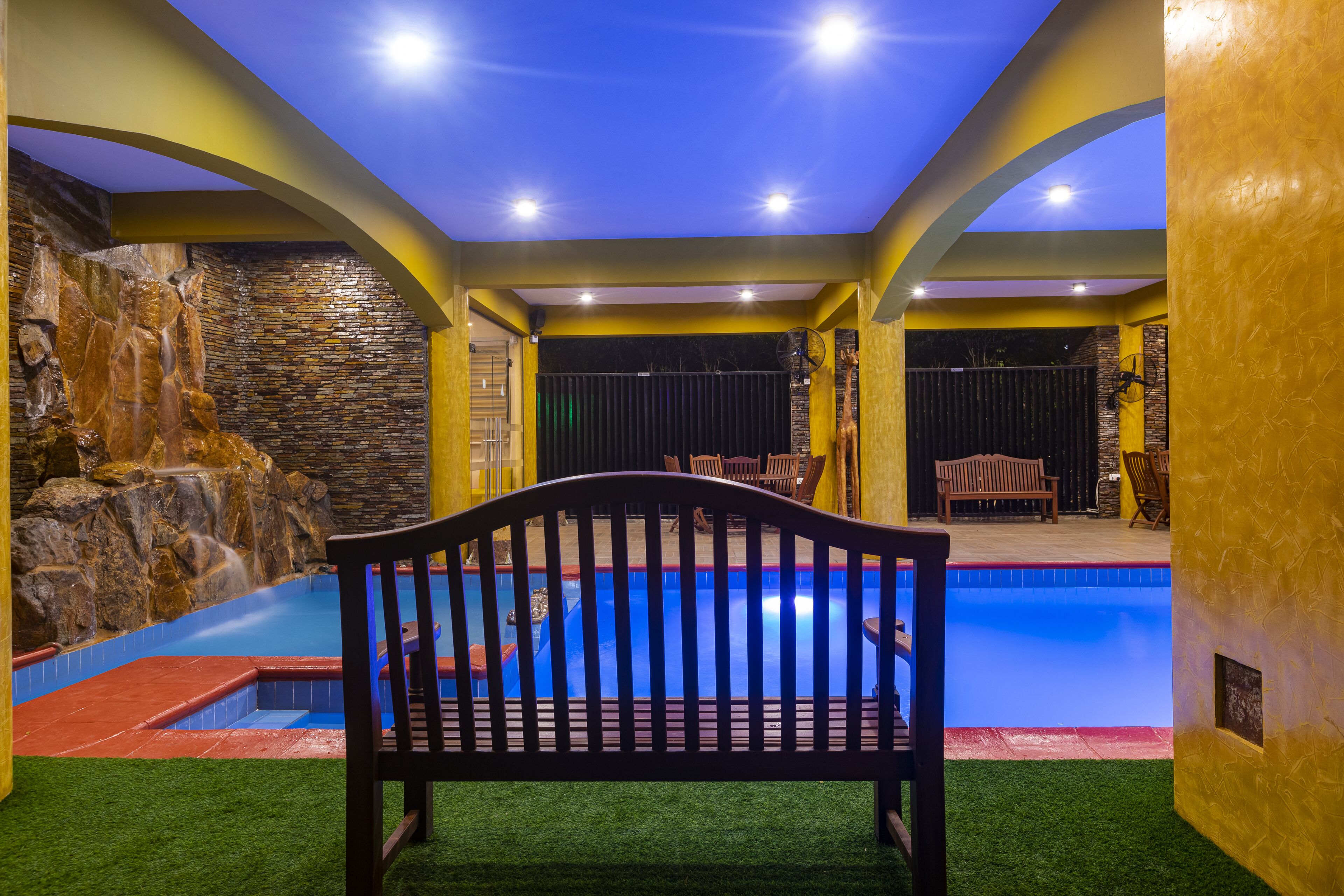 A pool area with a bench, a waterfall feature, and a stone wall.