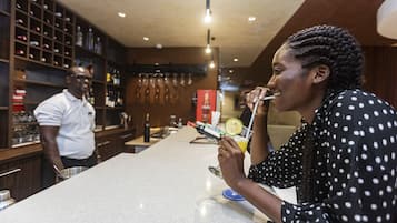 A bar area with a polished countertop, shelves with bottles, and a person holding a drink.