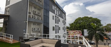 Un área de lounge en la azotea con mobiliario exterior, vistas a un edificio moderno y una palmera.