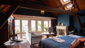 Un dormitorio con una cama grande, chimenea, mesa de comedor y vista al exterior.