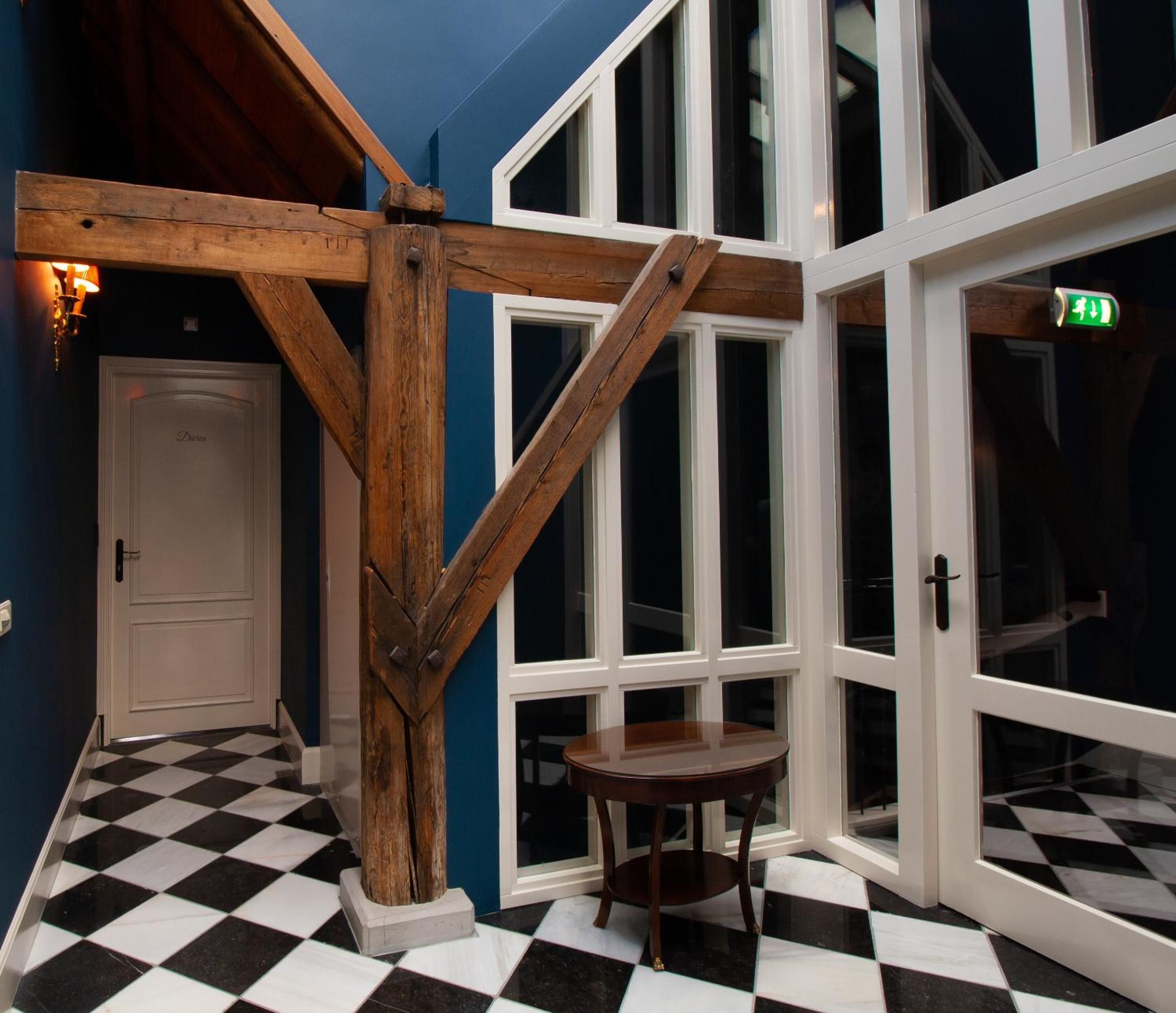 A room with a checkered floor, a wooden beam structure, a white door, and a large window.