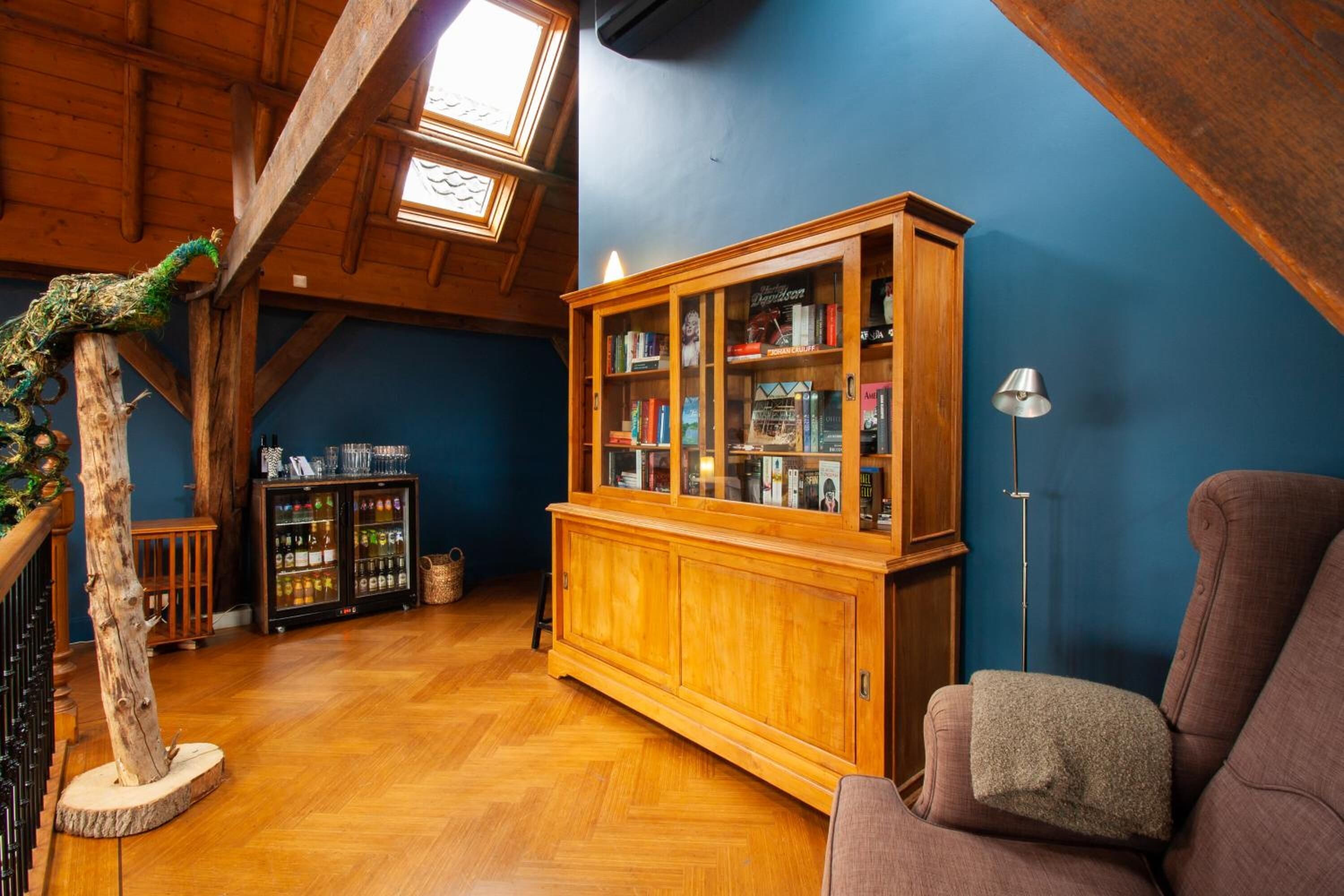 A room with a wooden cabinet, a bookshelf, a wooden chair, and a decorative tree.