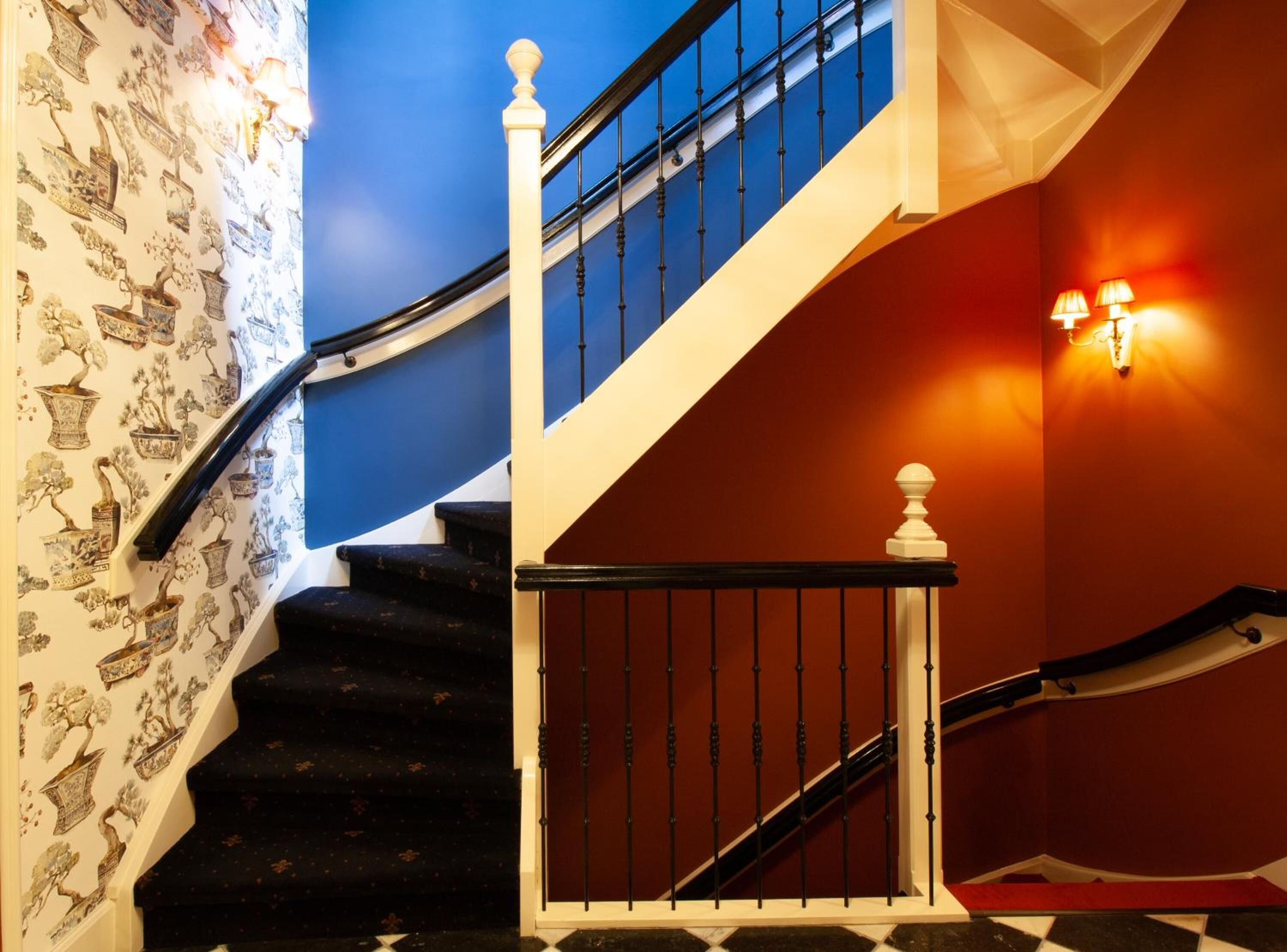 A staircase with black steps, white balusters, and a blue wall with a floral wallpaper.