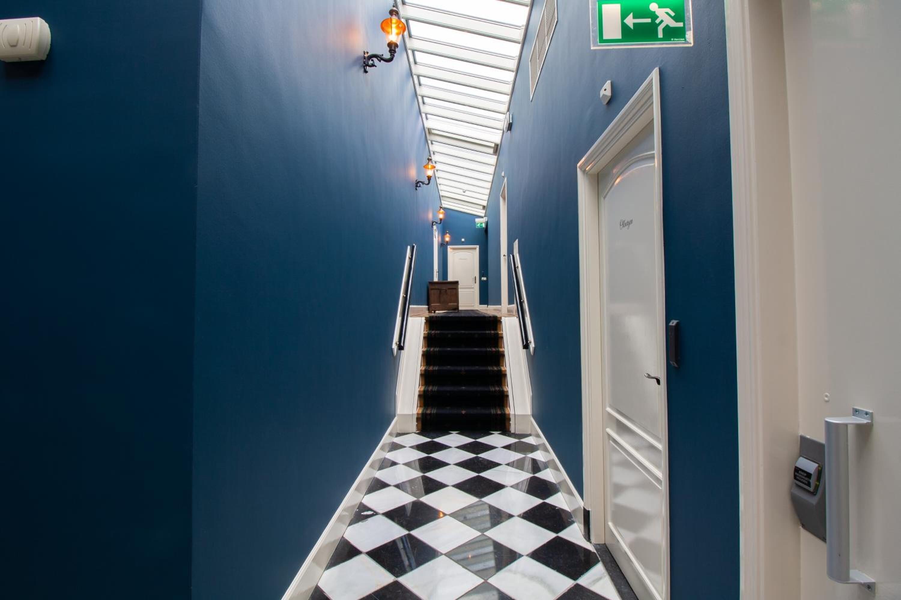 A hotel hallway with a checkered floor, blue walls, and a skylight.