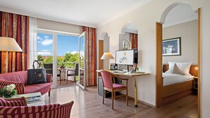 Ein Hotelzimmer mit Bett, Schreibtisch mit Computer, Stuhl, Sofa und Blick ins Freie.