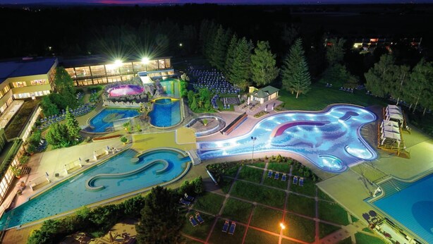 Eine Vogelperspektive eines Resorts mit mehreren Schwimmbecken, einem Wasserpark und einem großen Gebäude mit hellen Lichtern.