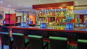 Eine Bar mit einer Marmor-Arbeitsplatte, mehreren Spirituosenflaschen und grünen Sitzmöbeln.