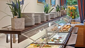 Ein reichhaltiges Buffet mit verschiedenen Speisen, darunter Fleisch, Käse und Gemüse, präsentiert auf einem langen Tisch mit einer Glasvitrine.