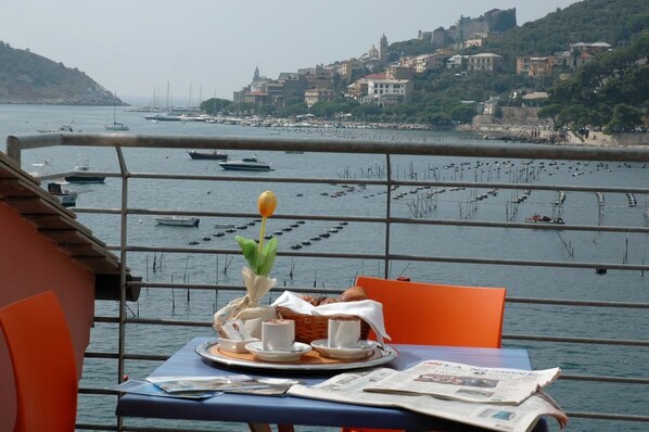 A table with a breakfast setup, overlooking a marina with boats and a hillside town.