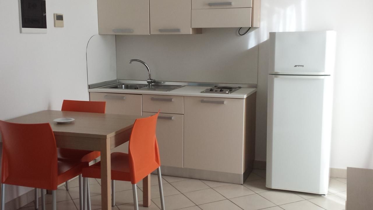 A compact kitchen with a sink, stove, and white refrigerator. There are two orange chairs around a small dining table.