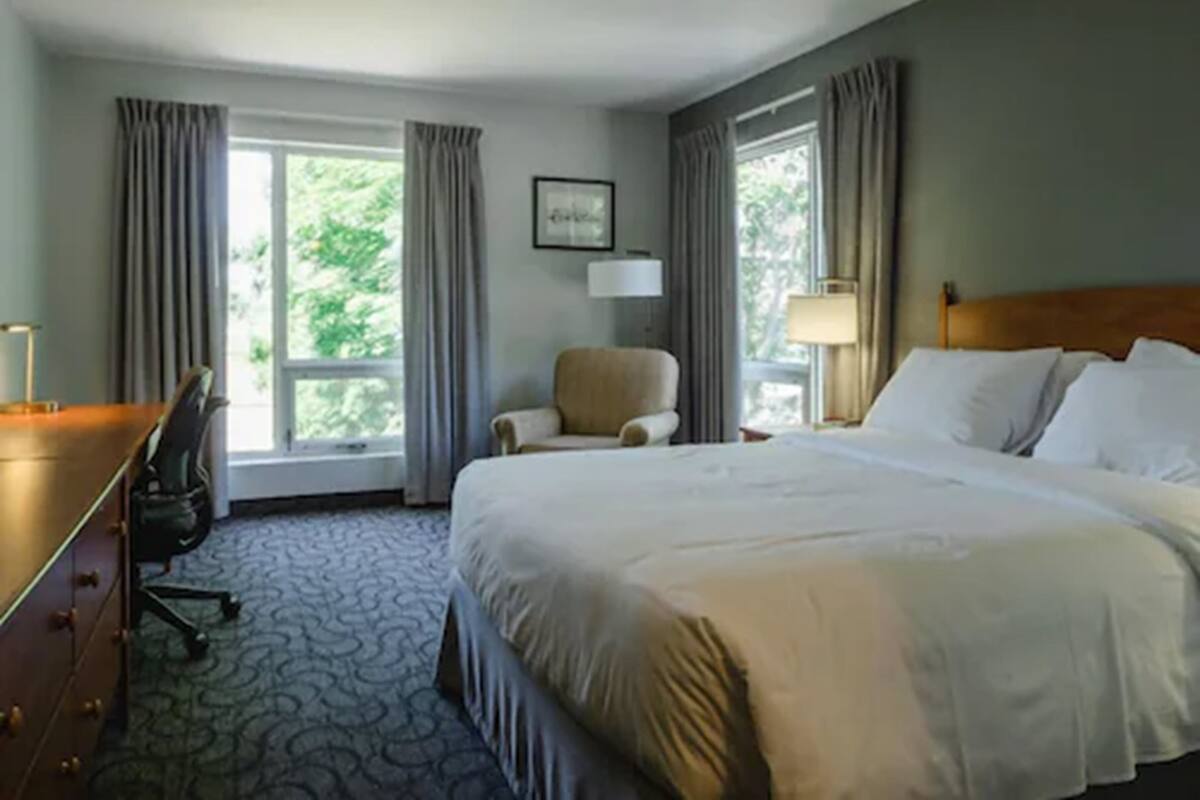 A hotel room with a large bed, a desk, a chair, and a window with curtains.