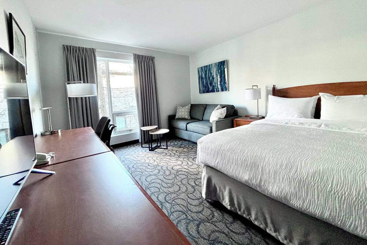 A hotel room with a large bed, a desk, a chair, a sofa, and a small table.