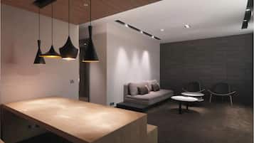 A modern interior with a wooden reception desk, black pendant lights, a grey sofa, and two chairs.