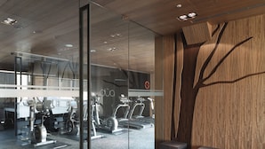 A modern gym with exercise equipment, glass walls, and a wooden accent wall with a tree design. - Hotel Dua (Kaohsiung)