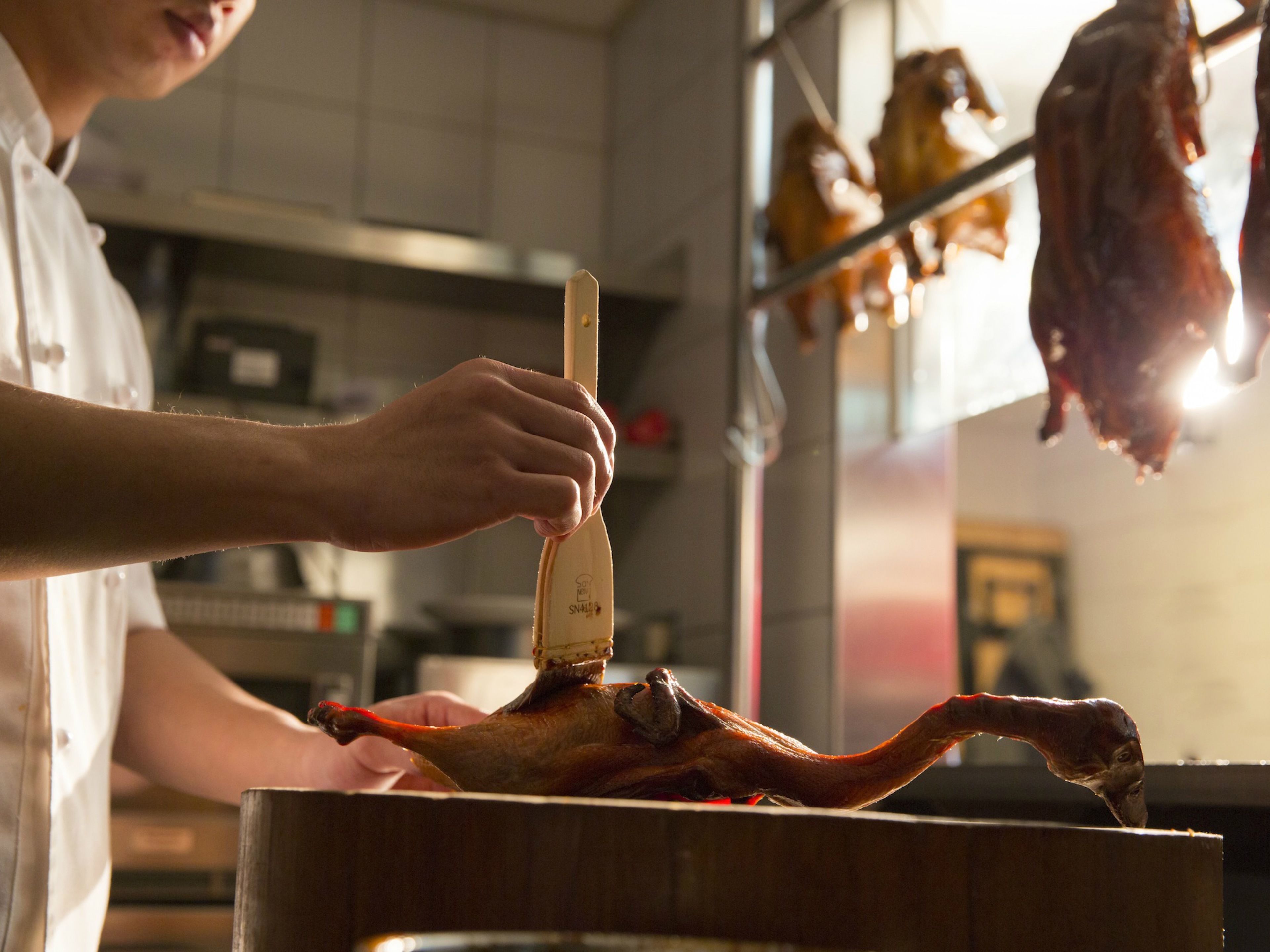A person carving a roasted duck in a kitchen.