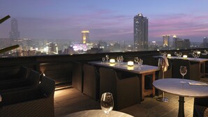 A rooftop dining area with tables and chairs, overlooking a city skyline at dusk. - Hotel Dua (Kaohsiung)
