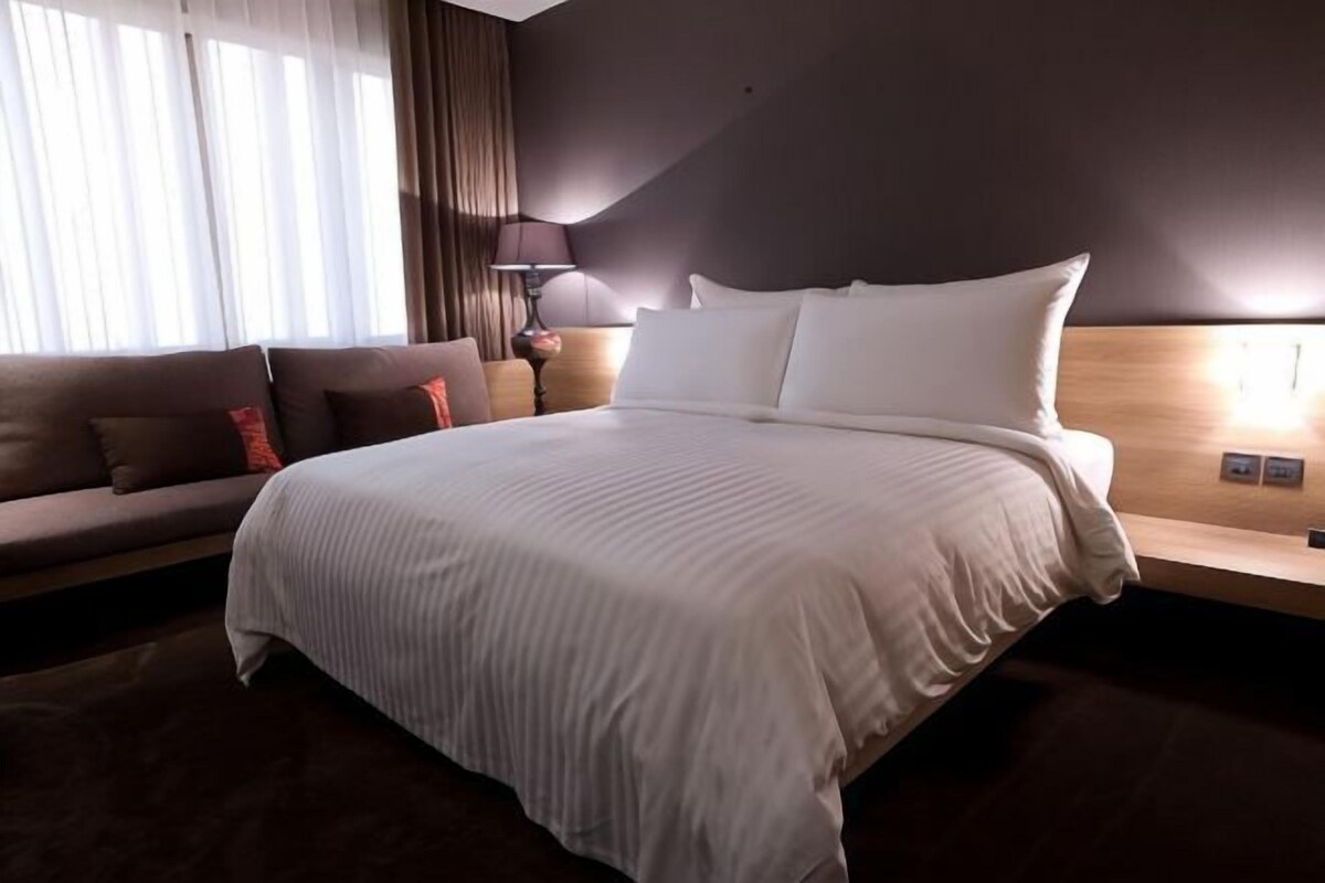 Une chambre d’hôtel avec un grand lit, un canapé, une lampe et une fenêtre avec des rideaux.