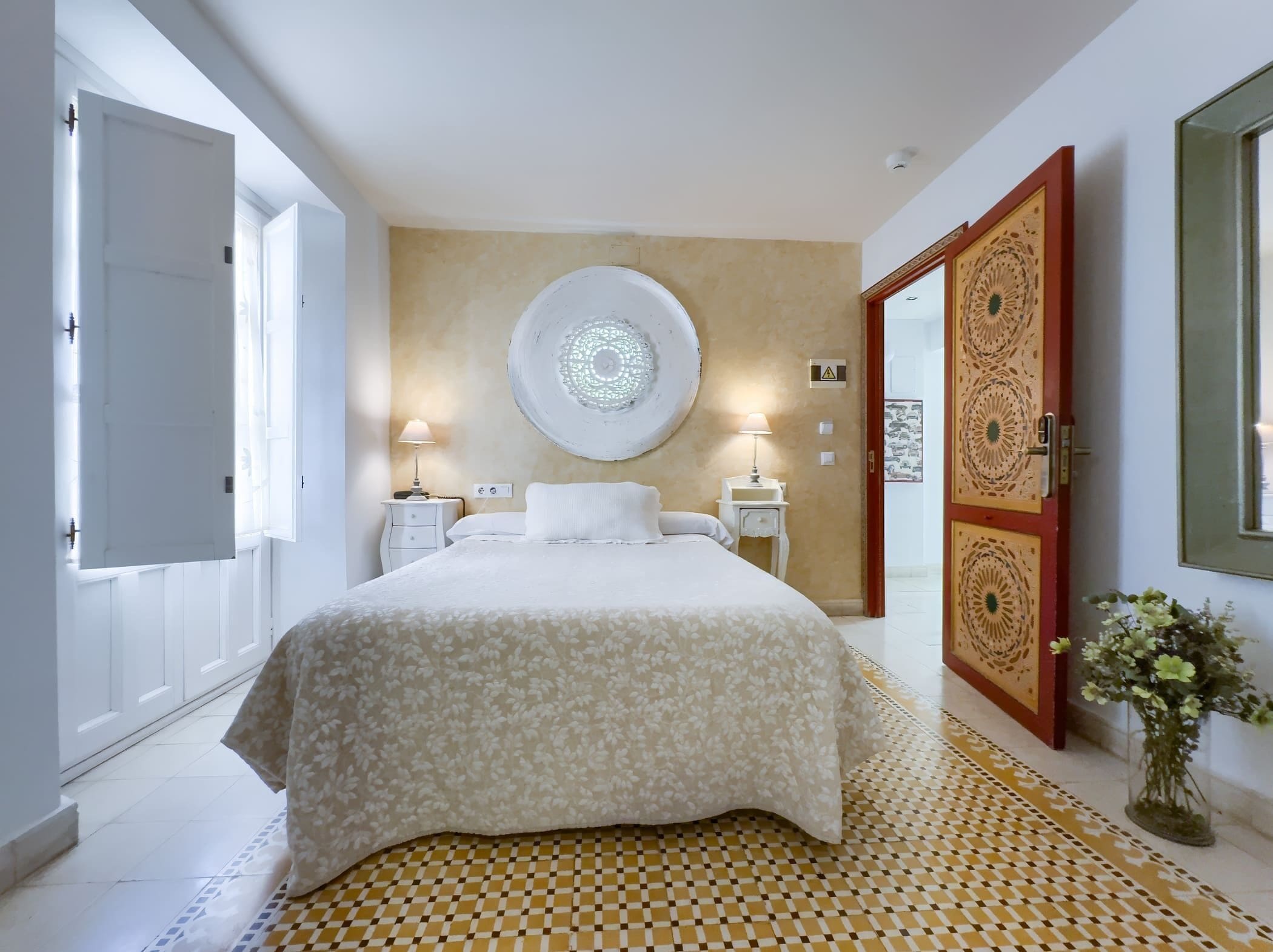 A bedroom with a large bed, two bedside tables with lamps, a round wall decoration, and a patterned rug.