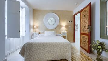 A bedroom with a large bed, two bedside tables with lamps, a round wall decoration, and a patterned rug.