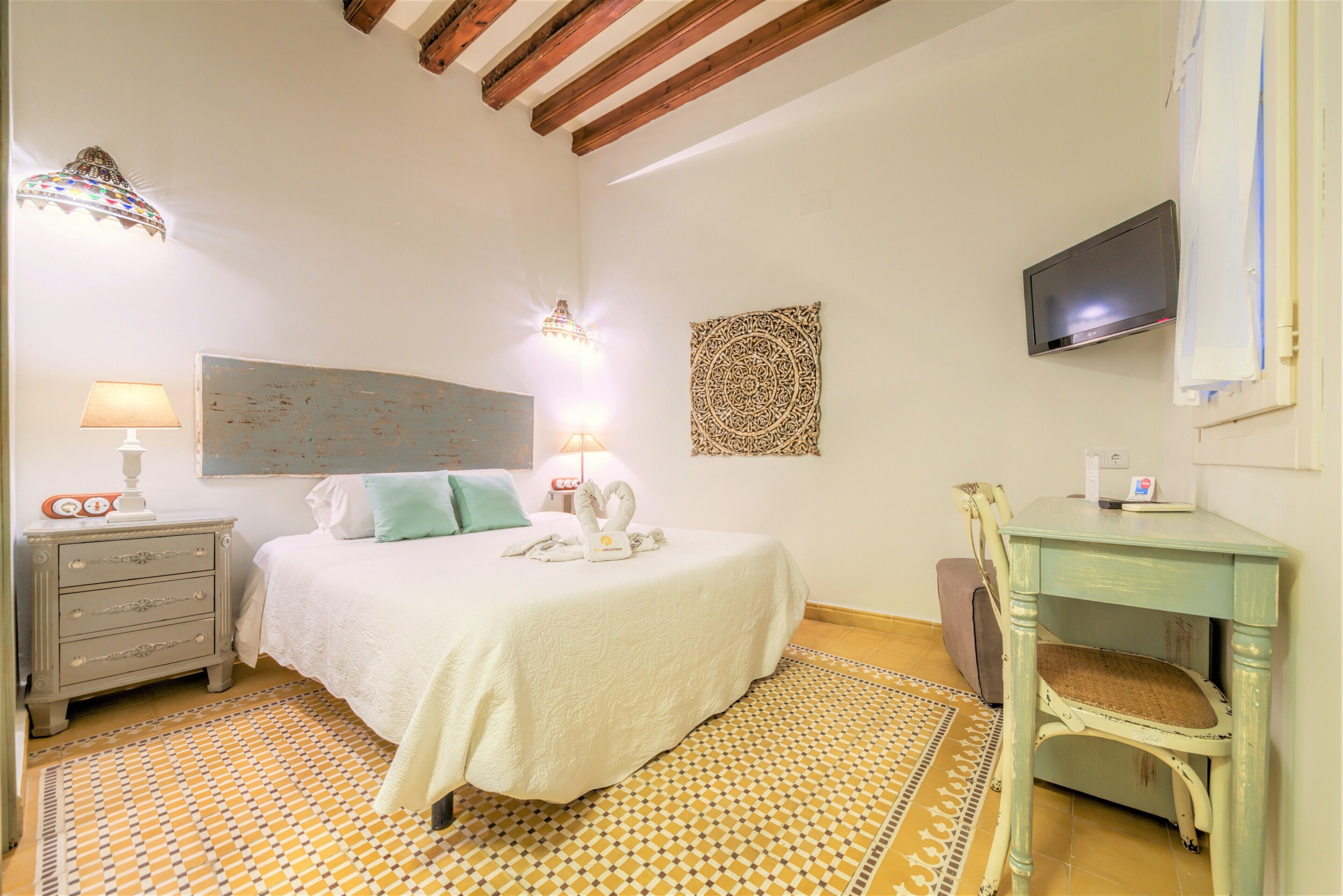 A bedroom with a bed, bedside lamps, a television, a desk, and a patterned rug.