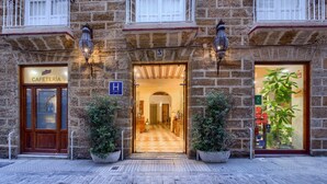 A stone building with a cafe entrance, a city sign, and a large potted plant. - Hotel Argantonio (Cádiz)