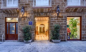 Un edificio de piedra con entrada de cafetería, un cartel de la ciudad y una planta grande en maceta.
