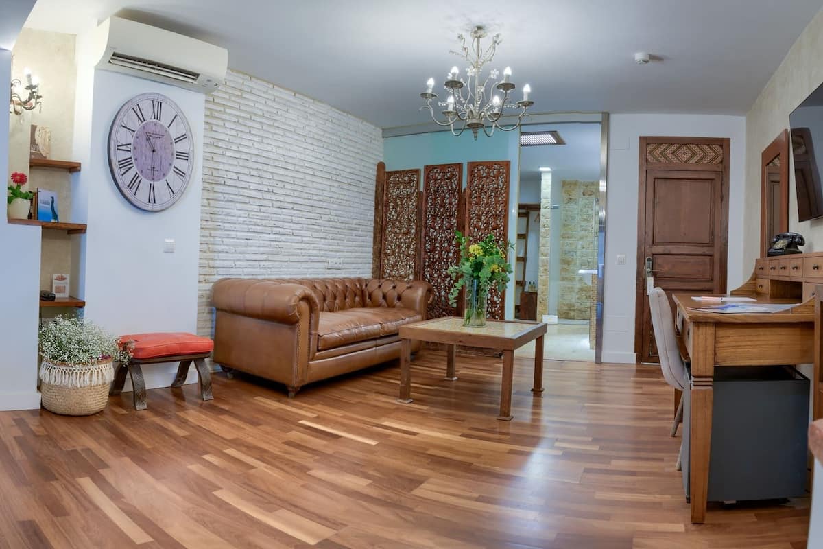 A living room with a brown leather sofa, a wooden coffee table, a large wall clock, and a chandelier.