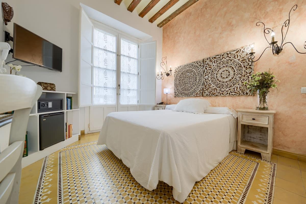 A bedroom with a large bed, a TV, a window, and a decorative wall piece.