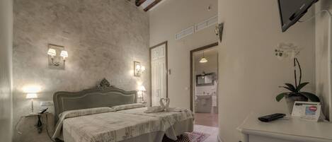 A hotel room with a bed, bedside lamps, a desk with a computer, and a bathroom visible through an open door.