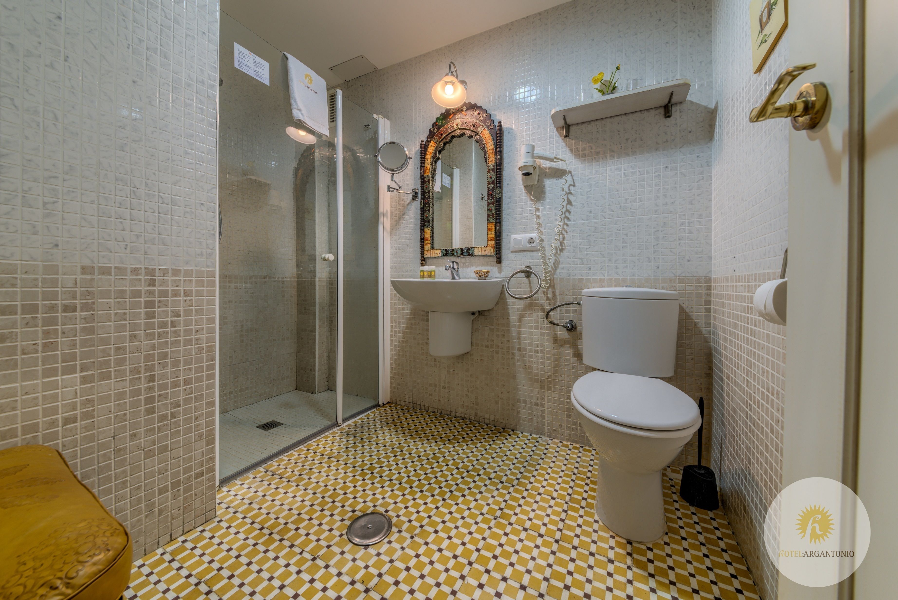 Une salle de bain avec un carrelage à motifs géométriques, un lavabo, des toilettes, une douche et un miroir.