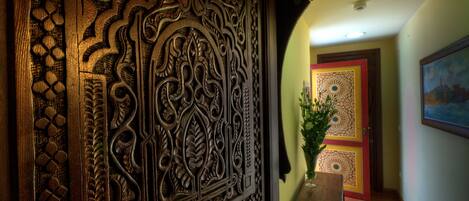 An ornate wooden panel with intricate carvings, a framed artwork on the wall, and a door with a geometric pattern.
