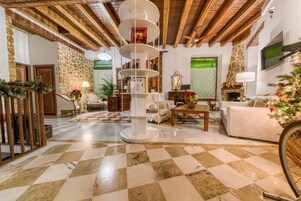 Amplia sala de estar con piso a cuadros, una estantería blanca central, vigas de madera en el techo, una pared de piedra y una chimenea.