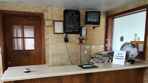 A reception desk with a wooden counter, a sign indicating Wi-Fi password, a television mounted on the wall, and a globe with a sign. - Budget Inn (Scottsboro)