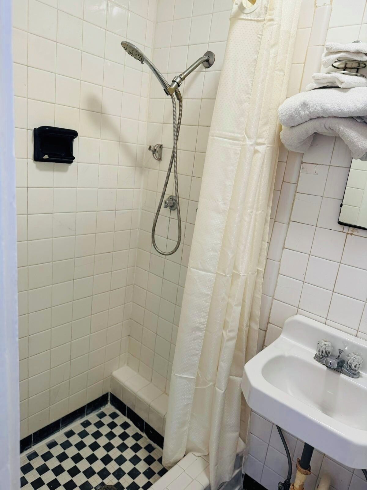 Un baño pequeño con ducha, lavamanos y suelo de baldosas.