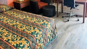 A hotel room with a large bed, a desk, a chair, and a lamp. - Budget Inn (Scottsboro)