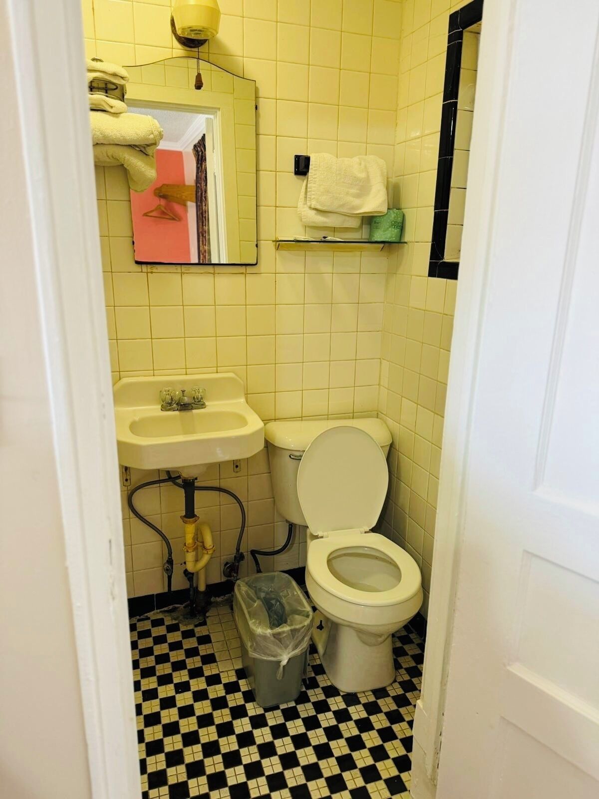 A small bathroom with yellow tiles, a white sink, a toilet, and a black and white checkered floor.