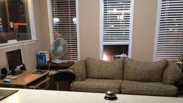 A living room with a sofa, a desk with a computer, and a fan. - Budget Inn (Scottsboro)