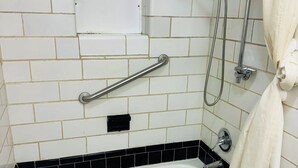 A bathroom with a white bathtub, a shower with a handheld showerhead, a grab bar, and a towel hanging on the wall. - Budget Inn (Scottsboro)
