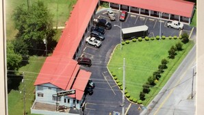 An aerial view of a parking lot with several cars, a building with a red roof, and a sign that reads "Budget Inn." - Budget Inn (Scottsboro)
