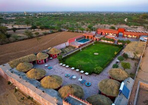A hotel with a swimming pool, thatched-roof huts, and a well-maintained lawn.