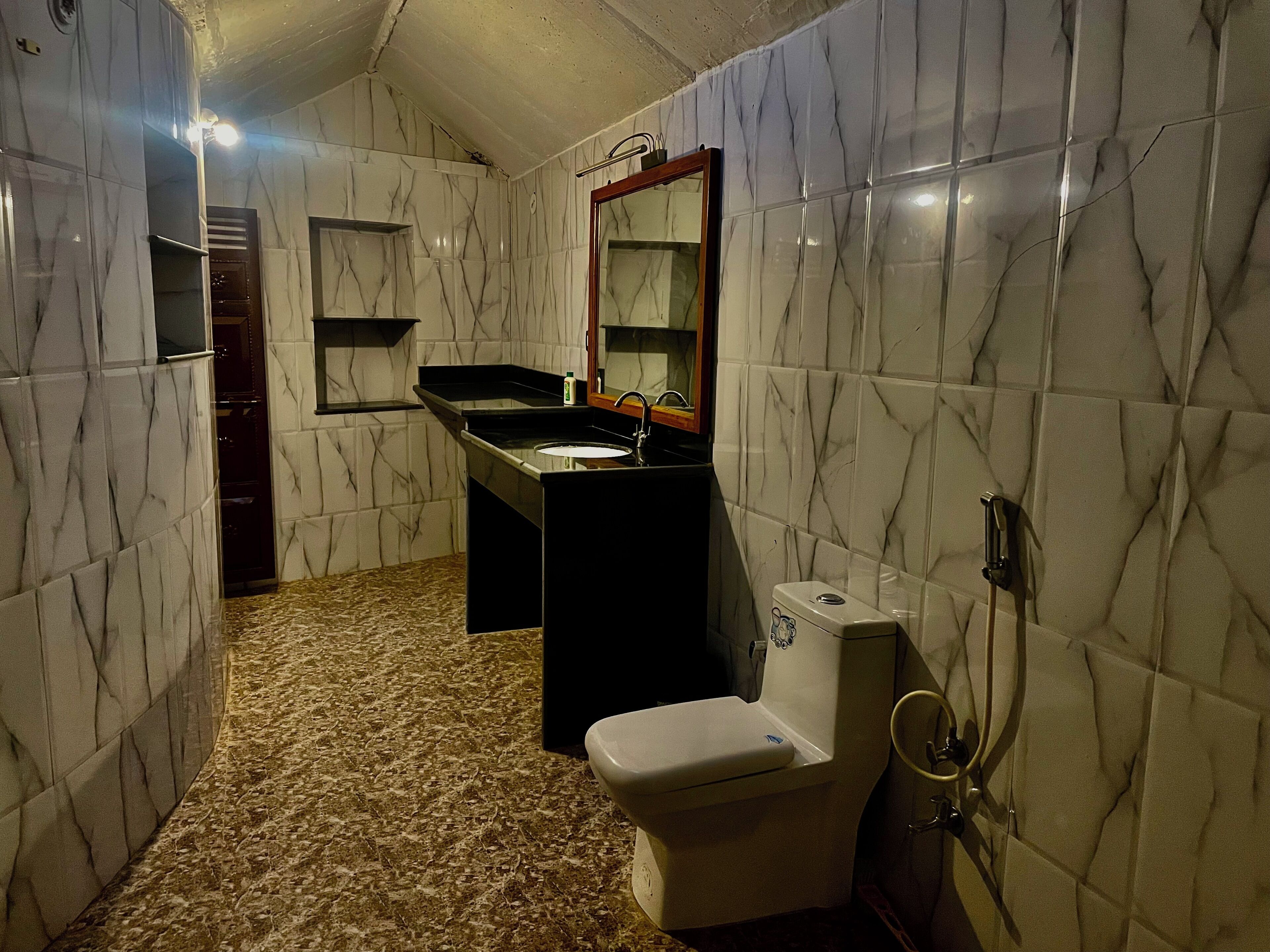 A bathroom with marble walls, a sink, a toilet, and a mirror.